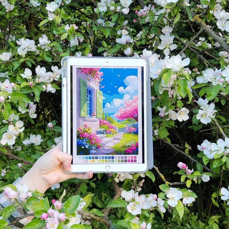 iPad with a colorful garden coloring page held in front of a blossoming apple tree