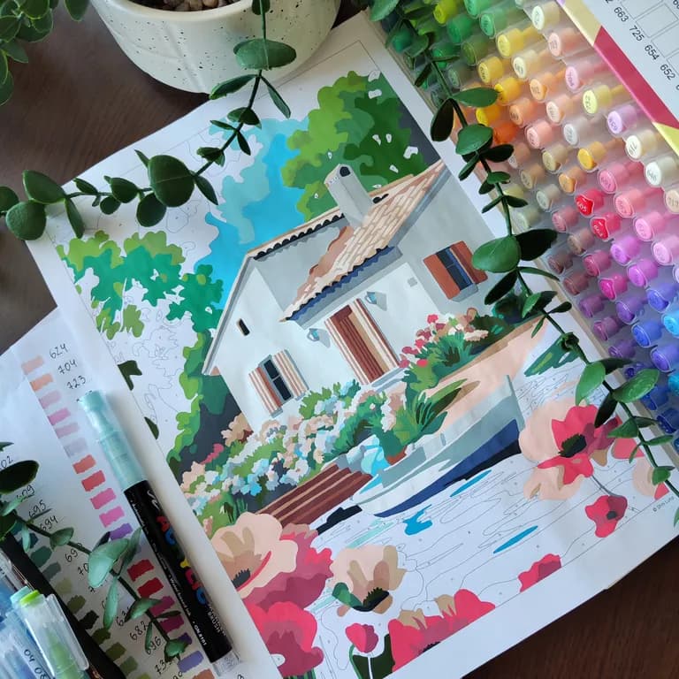 Half-colored cottage coloring page next to a large set of numbered markers